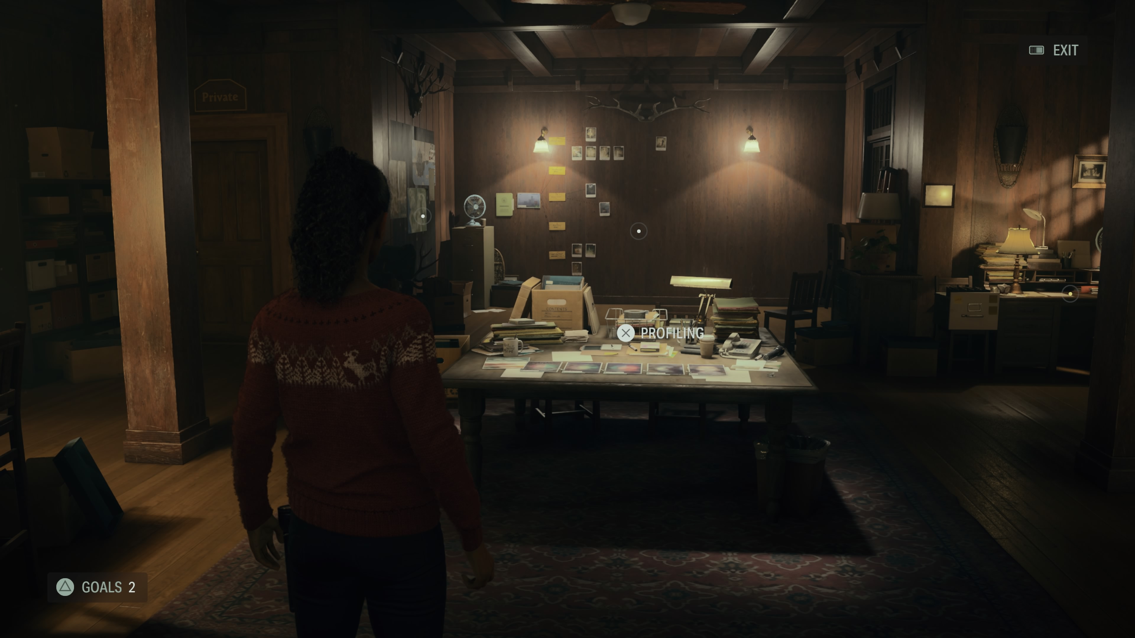 Screenshot of the Alan Wake II video game showing the player character in a room full of boxes and documents. On the screen are several interaction indicators, one which has the PlayStation X symbol on it.