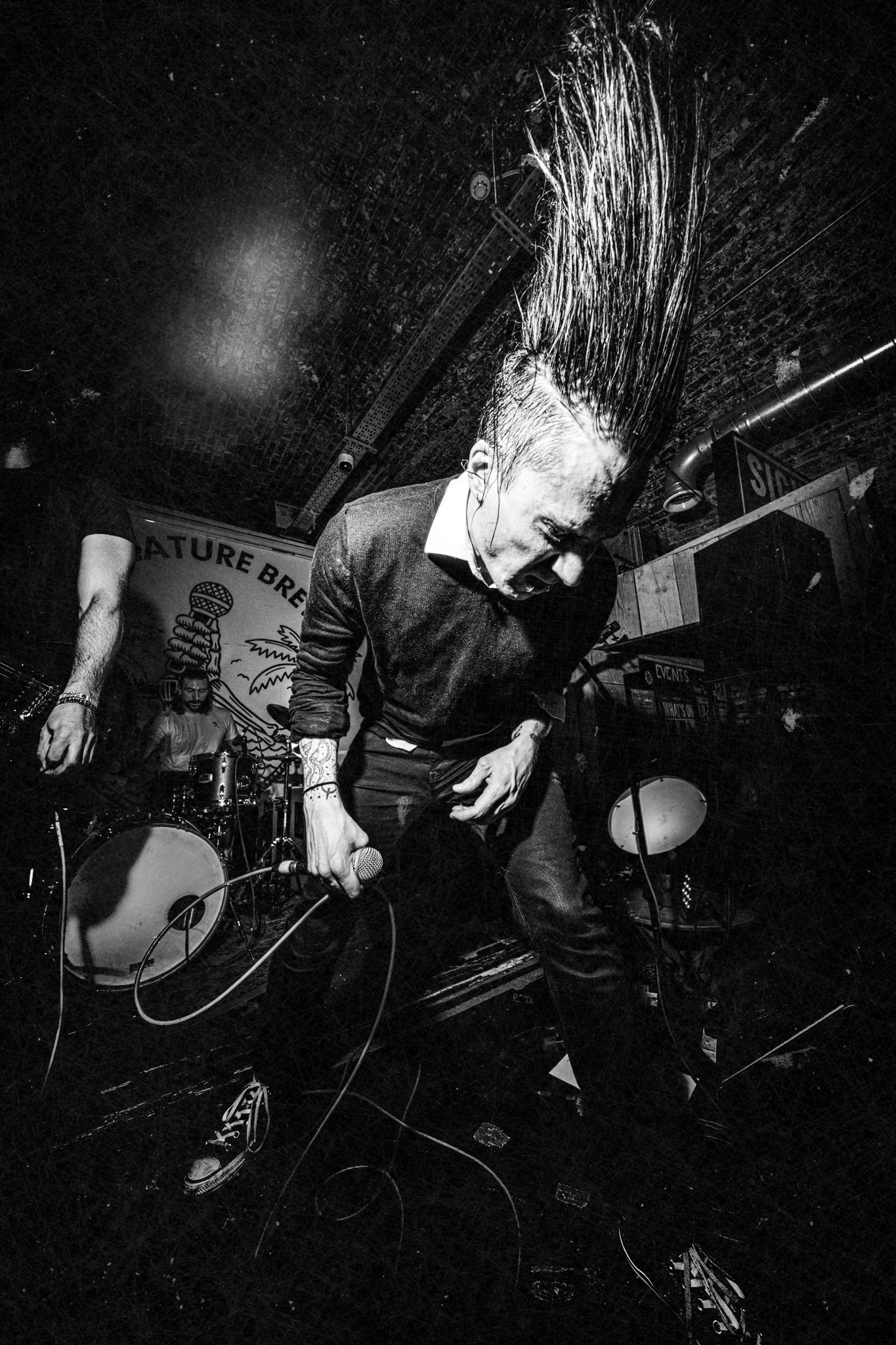 A black and white photo of me throwing my hair around on stage. On one side you see a bit of the guitar player and the drummer can be seen in the back.